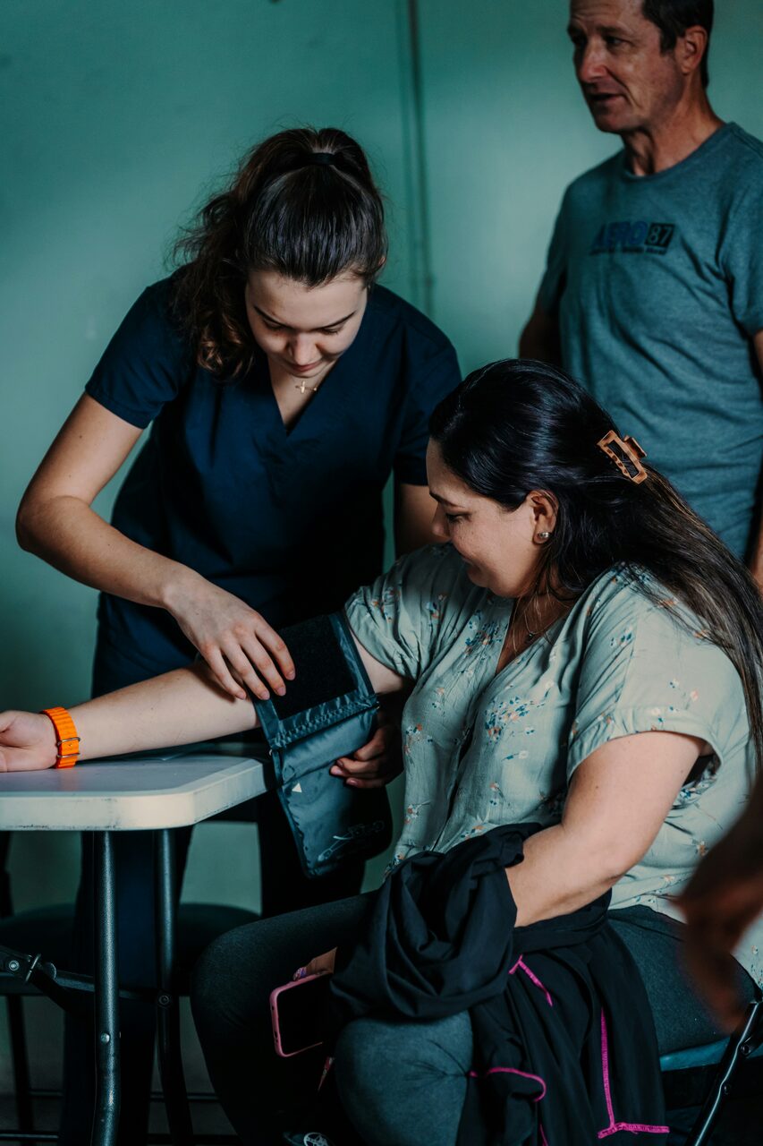 A health worker fitting a blood-pressure cuff on a seated woman's arm